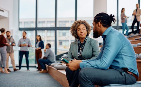 Two diverse people talking to each other while sitting on the first level of an auditorium