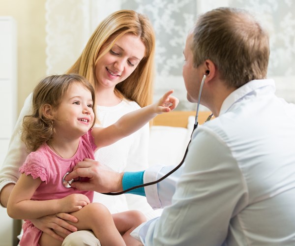Doctor with stethoscope listening to a heart of a small child who is being held by her mother